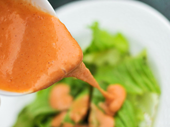 A cup of french dressing being poured over a salad